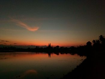 Silhouette trees by lake against sky during sunset