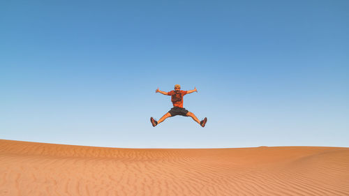 Man jumping in desert against clear sky