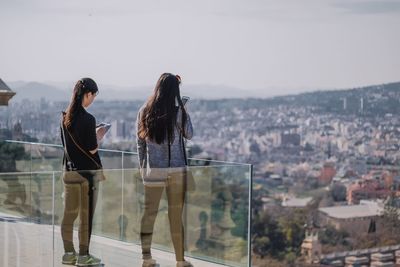 Rear view of women standing by cityscape against sky