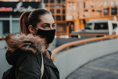 Young woman wearing mask looking away while standing in city