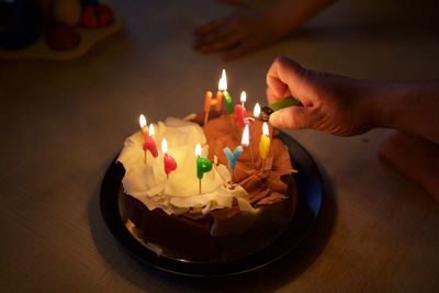 Cropped hand lighting birthday candles on cake at home