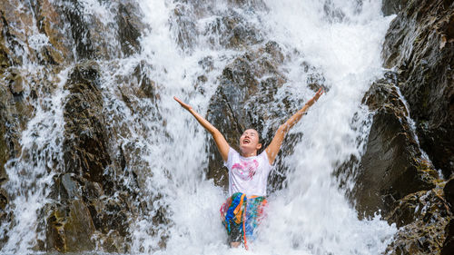 Young man splashing water in waterfall