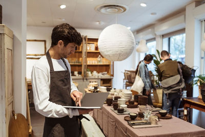 Owner analyzing digital tablet while customers choosing from merchandise at boutique