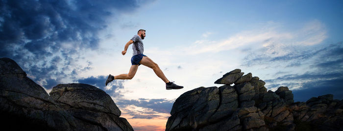 Low angle view of man jumping on rock against sky