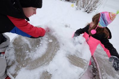 High angle view of sibling cleaning snow on table during winter