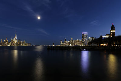 Illuminated buildings by river against sky at night