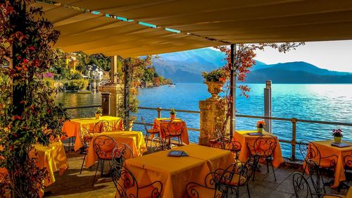 Chairs and tables at restaurant by sea against sky