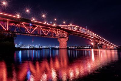 Illuminated bridge over river against sky in city at night