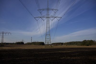 Low angle view of electricity pylon on field against sky