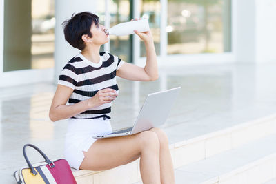 Side view of young woman using mobile phone while sitting at home