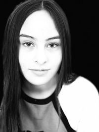 Close-up portrait of smiling young woman against black background