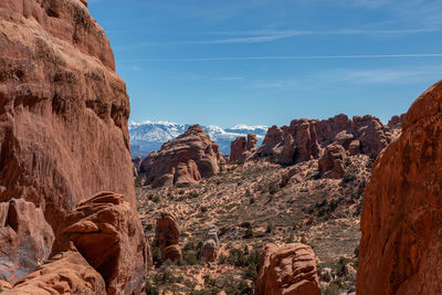 Red sandstone rock formations against sky with snow capped mountains in the background