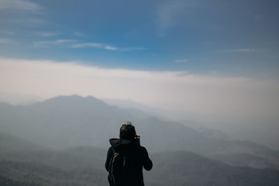 Rear view of man photographing landscape against cloudy sky