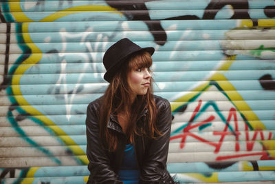 Portrait of young woman standing against graffiti