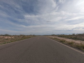 Empty road amidst field against sky