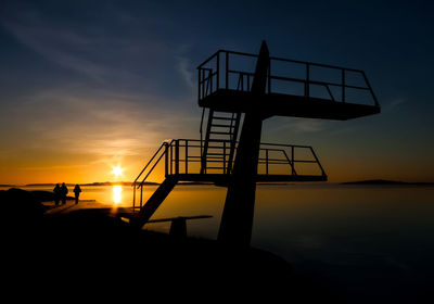 Silhouette diving platform by sea against sky during sunset