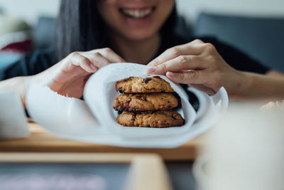 Smiling woman wrapping cookie in paper at home