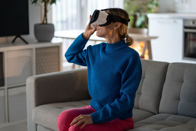 Young woman in vr glasses exlores virtual world with excited and amused expression at home