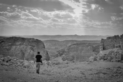 Rear view of man walking on mountain against sky