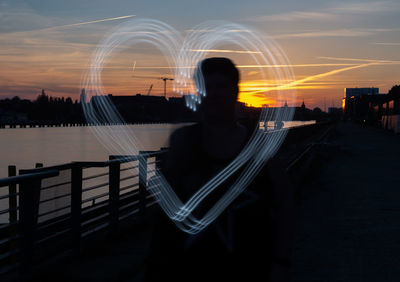 Blurred motion of silhouette person by illuminated city against sky during sunset