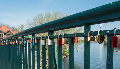 Close-up of padlocks on railing by river against sky