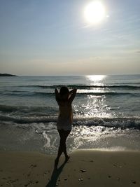 Rear view of woman standing on beach against sky during sunny day