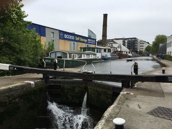 River flowing by buildings in city against sky