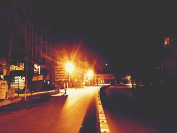 Illuminated road in city against clear sky at night