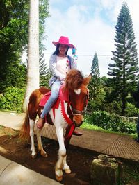 Portrait of smiling young woman horseback riding against trees