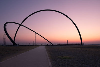 Road by silhouette bridge against sky during sunset