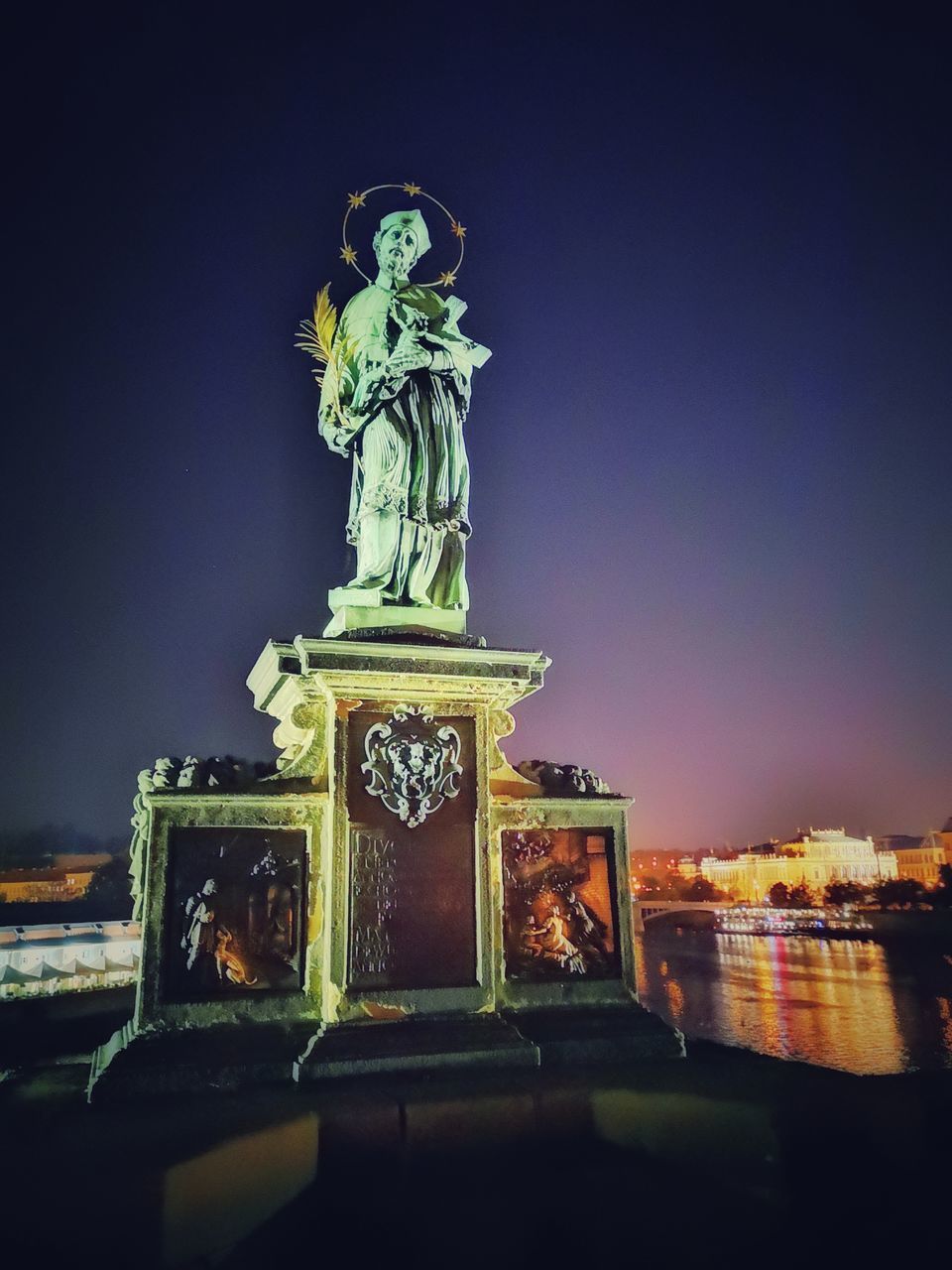 STATUE AGAINST ILLUMINATED CITY AT NIGHT