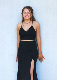 Portrait of smiling young woman wearing black dress standing against wall