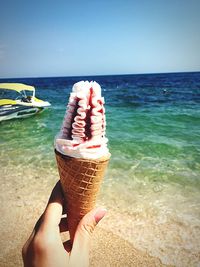 Midsection of person holding ice cream in sea against sky