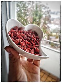 Cropped hand holding goji berries n in bowl at home