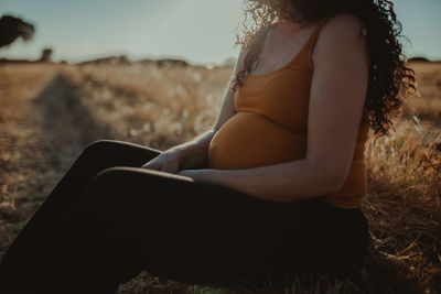 Midsection of pregnant woman sitting on field