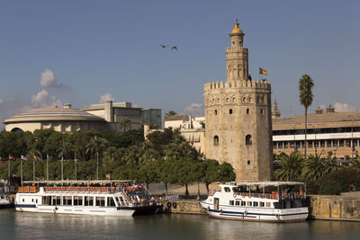 Ferries moored in river by torre del oro against sky