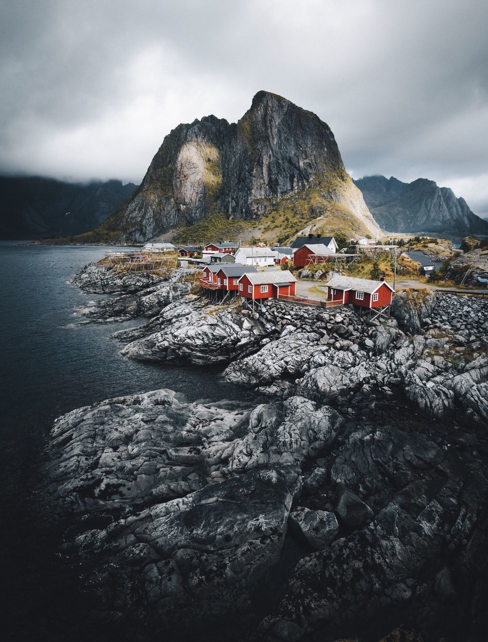 mountain, beach, water, mountain range, sky, tranquil scene, tranquility, nature, outdoors, shore, cloud - sky, day, scenics, beauty in nature, sea, mountain peak, non-urban scene, human settlement, rock formation, coastline, rural scene, remote, wave, cliff