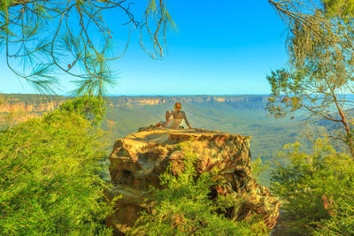 Rear view of woman sitting on rock against landscape