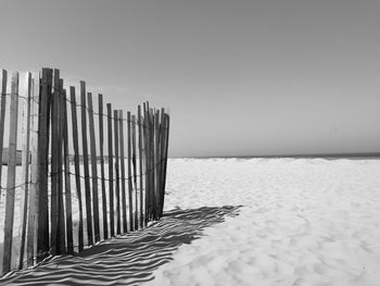 Wooden fence ans horizon line on beach against clear sky