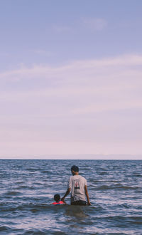 Man sitting in sea against sky during sunset