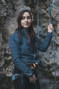 Portrait of young woman holding climbing rope while standing by mountain