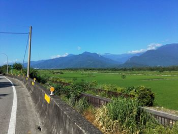 Road amidst field against clear blue sky