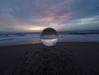 Water on rock at beach against sky during sunset