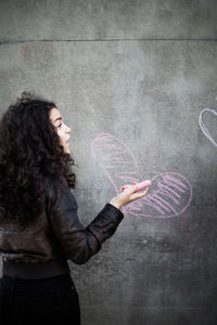 Rear view of teenage girl drawing heart shape on wall with pink chalk