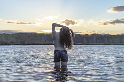 Rear view of shirtless woman standing in lake against sky