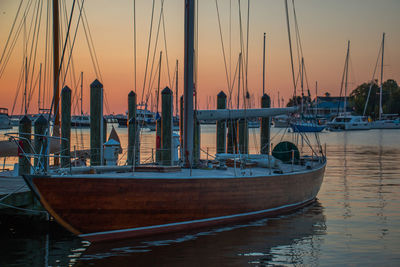 Sailboats moored in harbor at sunset