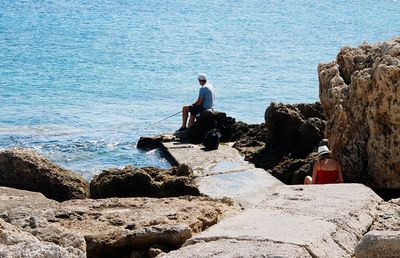 Man standing on rock by sea against sky