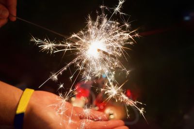 Cropped hands of person holding burning sparkler at night