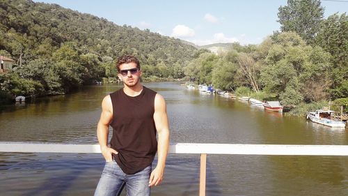 Portrait of young man standing at railing against lake