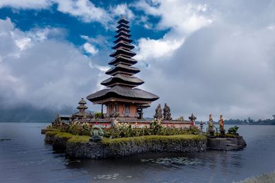 Temple in lake against cloudy sky